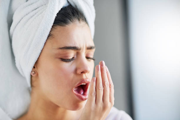 a woman with a towel wrapped around her head, trying to smell her breath